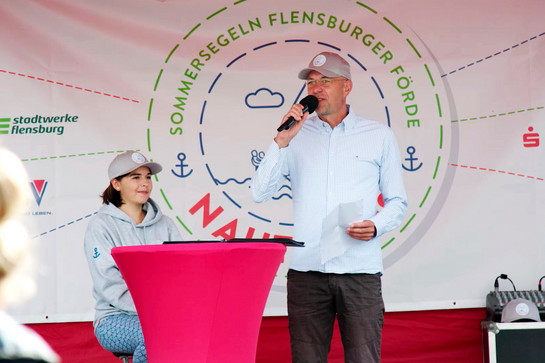 Ein Mann mit Cappy hält eine Rede auf einer Bühne
