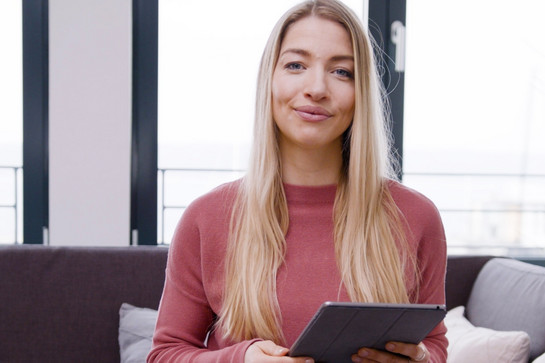 Eine blonde Frau im pinken Shirt hält ein Ipad