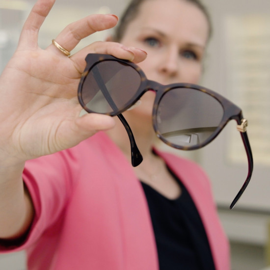 Eine Frau im pinken Shirt hält eine Sonnenbrille in die Kamera