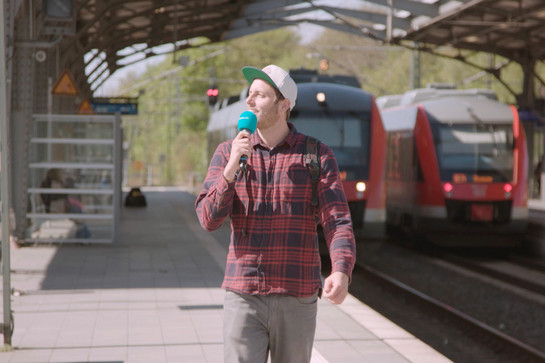 Ein Mann geht mit einem Mikro am Bahnsteig lang