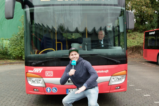 bb_festtagsgruesse_teaser_02.jpg Ein Mann mit Mikrofon posiert vor einem roten Bus