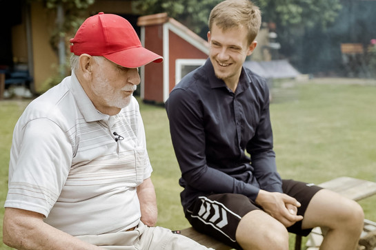 bb_kuehta_folge_4_teaser_04.jpg Ein alter Mann mit einer roten Cappy unterhält sich mit einem jungen Mann