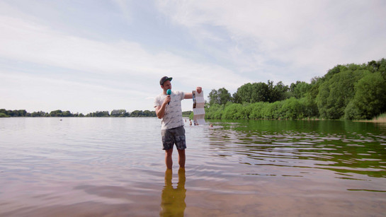 Lars steht im Wasser und hält einen Flyer in der Hand