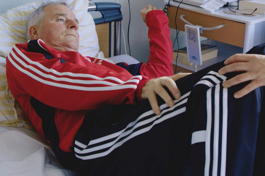 Ein älterer Mann im Jogginganzug liegt im Bett