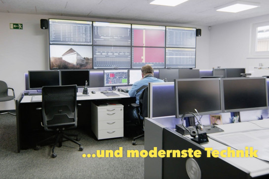 Mann sitzt in einem Raum voller Bildschirme auf Schreibtischen und an der Wand