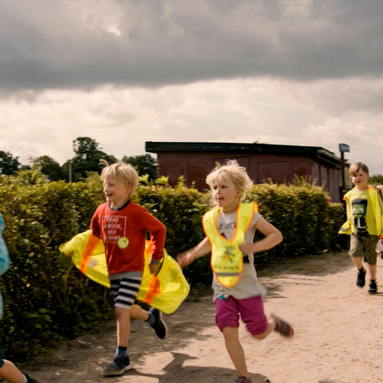 Mehrere Kinder laufen mit einer gelben schutzweste