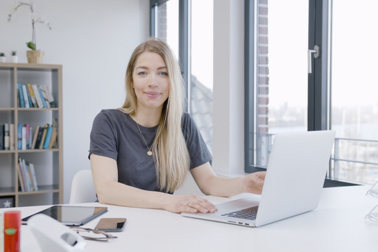 Eine Frau mit langen blonden Haaren sitzt vor einem grauen Laptop