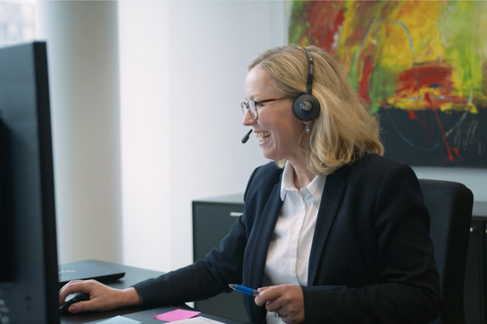 Blonde Frau am Schreibtisch sitzend mit Headset auf dem Kopf