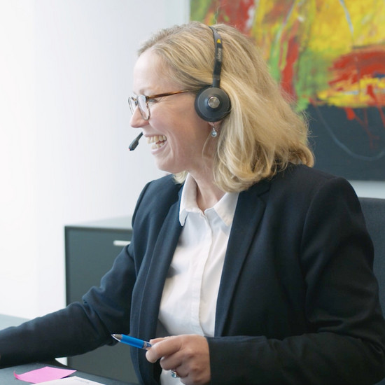 Blonde Frau am Schreibtisch sitzend mit Headset auf dem Kopf
