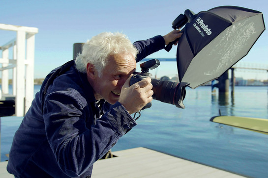 Mann fotografiert auf einem Holzsteg am Wasser