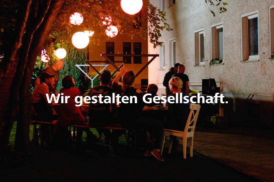 Eine Personengruppe sitzt Abends in einem Hinterhof und isst gemeinsam