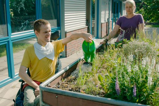 Ein Junge im Rollstuhl gießt die Blumen