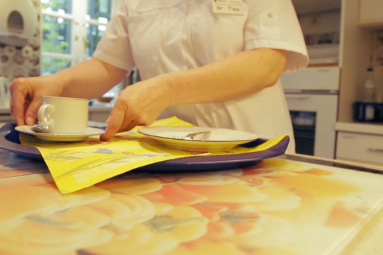 Eine Pflegerin stellt Teller und Tasse auf ein Tablett