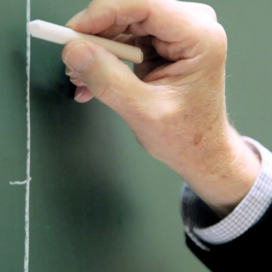 Ein Mann schreibt etwas mit Kreide auf eine Tafel