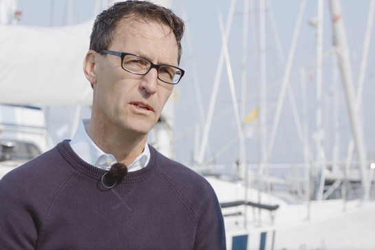 Testimonial Sven Christensen steht vor einem Segelboot, das im Hafen liegt.