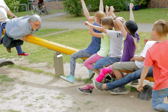 Kinder wippen mit zwei Erwachsenen auf einer gelben Wippe