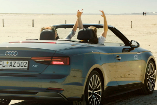 Zwei Frauen fahren in einem Audi Cabrio am Strand