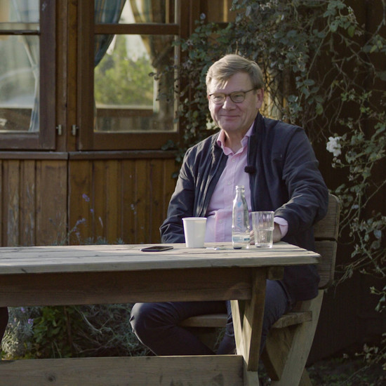 Ein Mann sitzt im Freien auf einem Holzstuhl im Garten