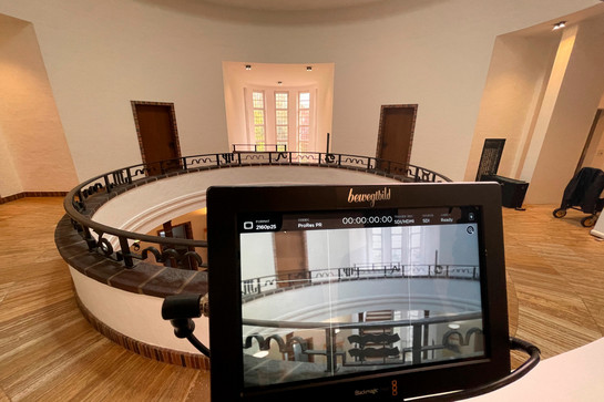 Ein runder, heller Raum mit Fenster und zwei Türen. Blick auf Kameradisplay 