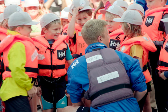 Kinder in roten Rettungswesten stehen um einen Mann herum