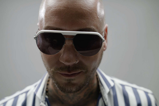 Mann mit Glatze und Nasenpiercing trägt große Sonnenbrille mit weißem Rahmen