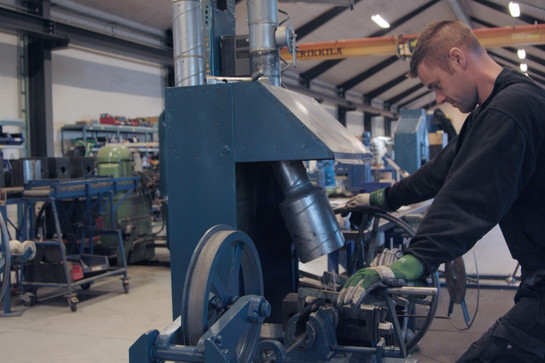 Ein Mann in Arbeitskleidung steht an einer großen Maschine in einer Halle. 
