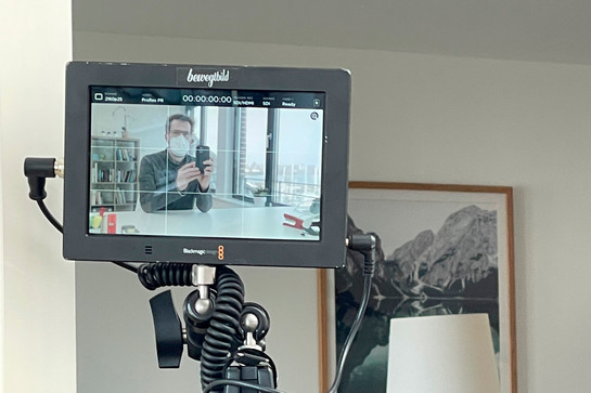 Ein Mann mit Mundschutz und Handy ist auf dem Bildschirm einer Kamera abgebildet