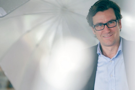 Mann mit Brille, er trägt ein hellblaues Hemd und lächelt.