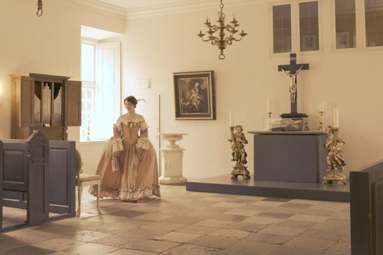 Eine Frau in einem rosanen Gewand geht durch die Kapelle des Schloss Husum