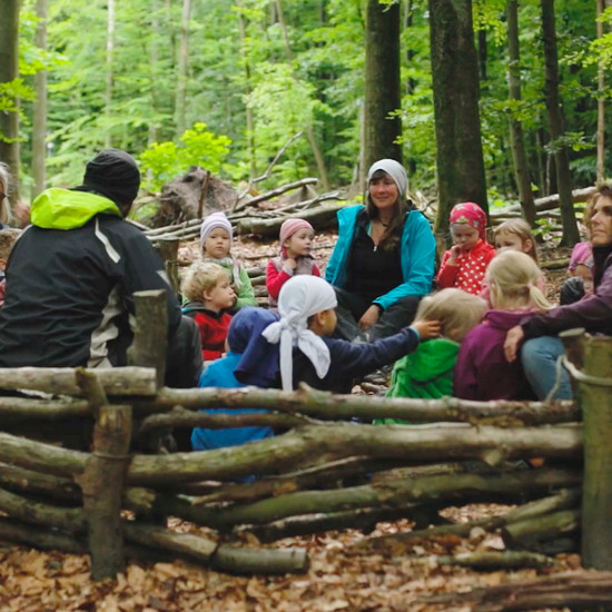 Kinder sitzen mit drei Betreuern im Wald
