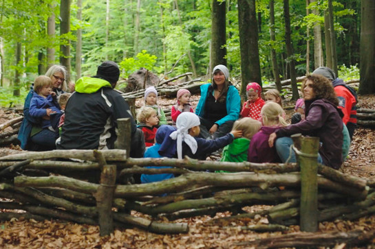 Kinder sitzen mit drei Betreuern im Wald