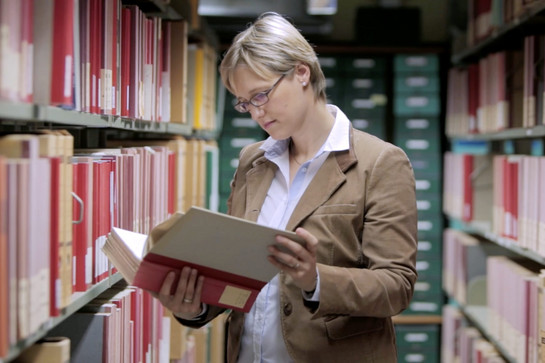 Eine Frau mit Brille schlägt ein Buch auf