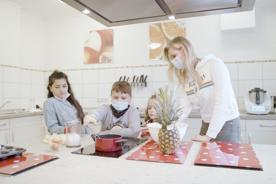 Eine Frau kocht mit drei Kindern in einer Küche