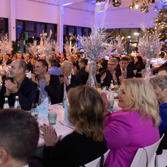 Veranstaltungssaal mit klatschenden Gästen an langen Tischen