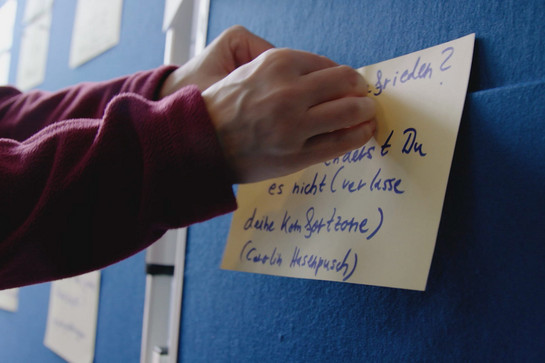 Eine Person klebt ein Blatt Papier an eine Pinnwand