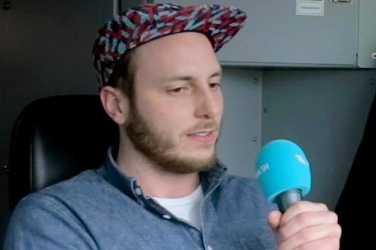 bb_fuehrerstand_teaser_04.jpg Ein Mann mit Cappy und Mikrofon sitzt in einem schwarzen Ledersitz