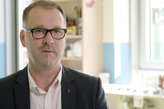 bb_kita_teaser_05.jpg Standbild von einem Mann mit schwarzer Brille