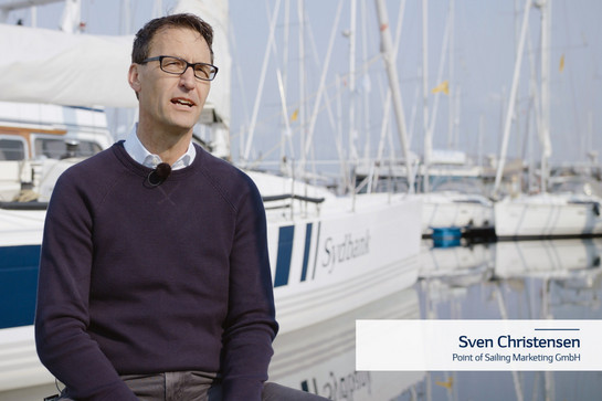 Testimonial Sven Christensen steht vor einem Segelboot, das im Hafen liegt.