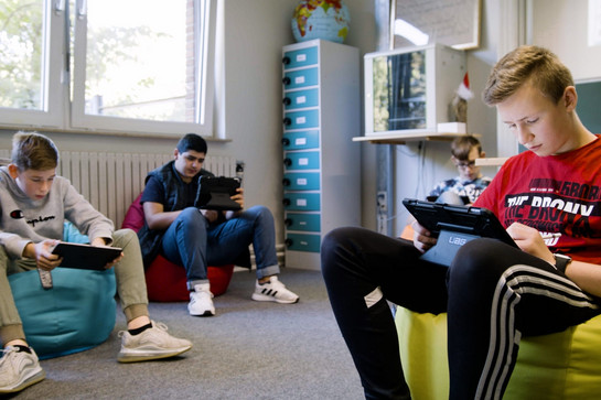Schüler sitzen in Sitzsäcken und tippen auf Ipads