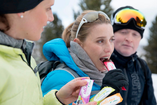 Drei Personen essen Energieriegel. Sie tragen Winterkleidung und Skibrillen. 