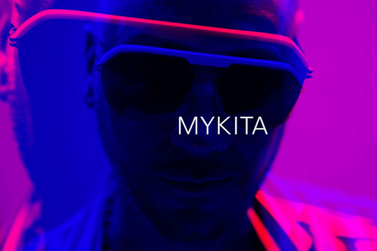Mann im dunklen Raum trägt Sonnenbrille, pinker Hintergrund, blaue Akzente