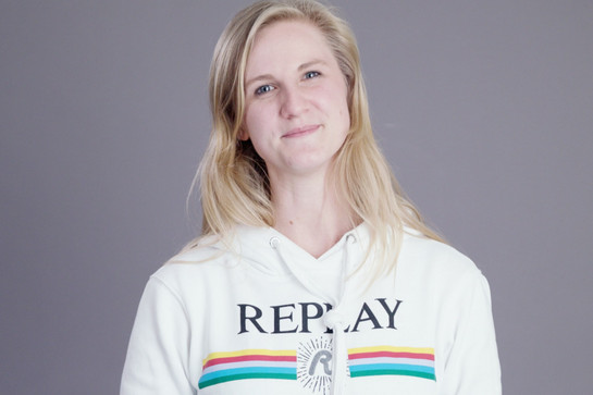 Eine blonde Frau im weißen Replay Pullover lacht in die Kamera