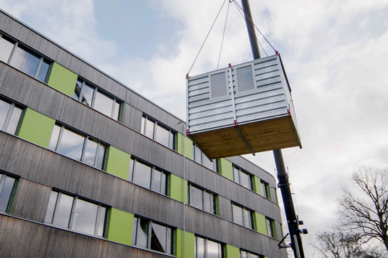 bb_sgm_teaser_05.jpg Kleiner Container hängt an Kran vor modernem Gebäude