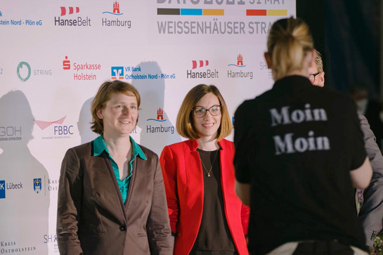 Zwei junge Menschen vor einer Leinwand mit Sponsorenlogos