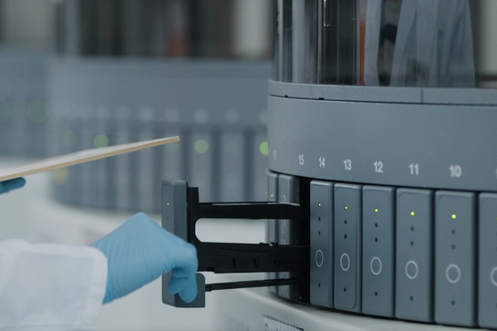 Ein Laborant entnimmt eine Probe aus einer grauen Maschine