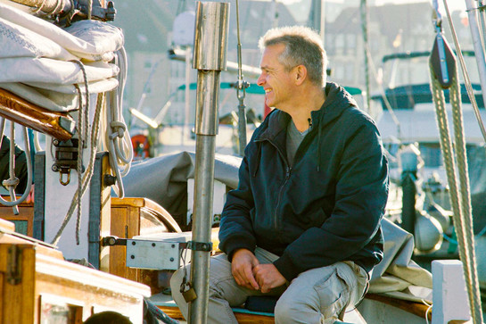 bb_stephan_teaser_06.jpg Stephan Hansen Oest sitzt lächelnd auf einem Boot