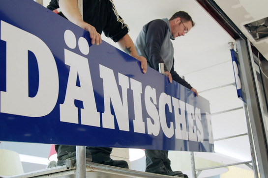 Zwei Handwerker hängen ein Schild auf vom dänsichen Bettenlager