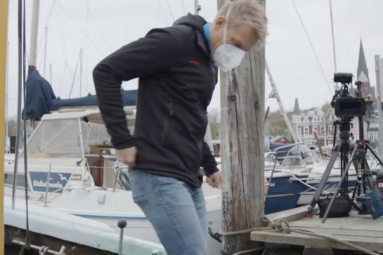 Ein Mann mit weißer Maske steht auf einem Flensburger Steg