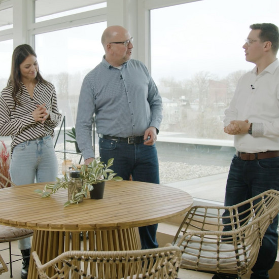 2 Männer und eine Frau stehen hinter einem runden Tisch und unterhalten sich