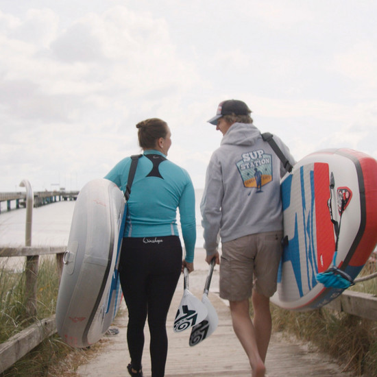 Zwei Personen gehen mit einem Sup ins Wasser